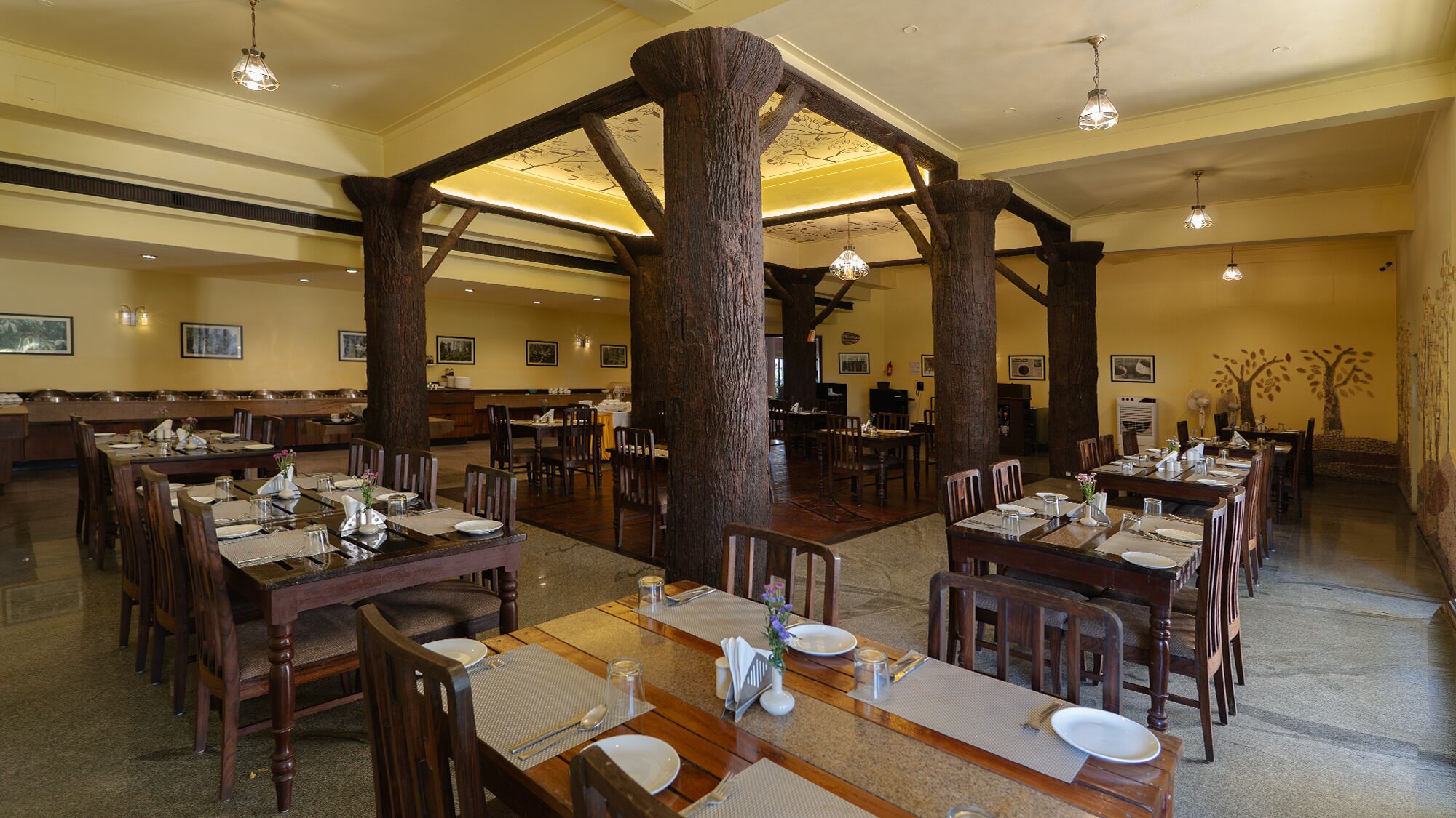 Une vaste salle à manger dotée de poutres en bois apparentes et de nombreuses tables dressées pour le repas.