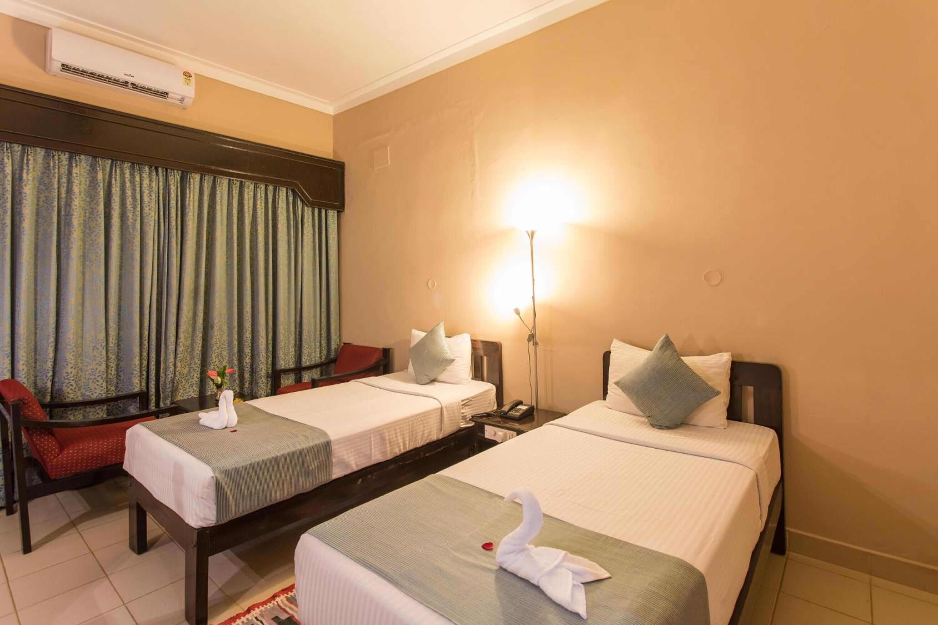 Ein Hotelzimmer mit zwei Einzelbetten, einem Schreibtisch, einem Stuhl und einer Lampe.