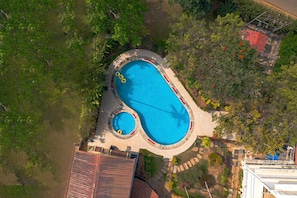Vista aérea de una propiedad residencial con una piscina grande, un jacuzzi circular y abundante vegetación.
