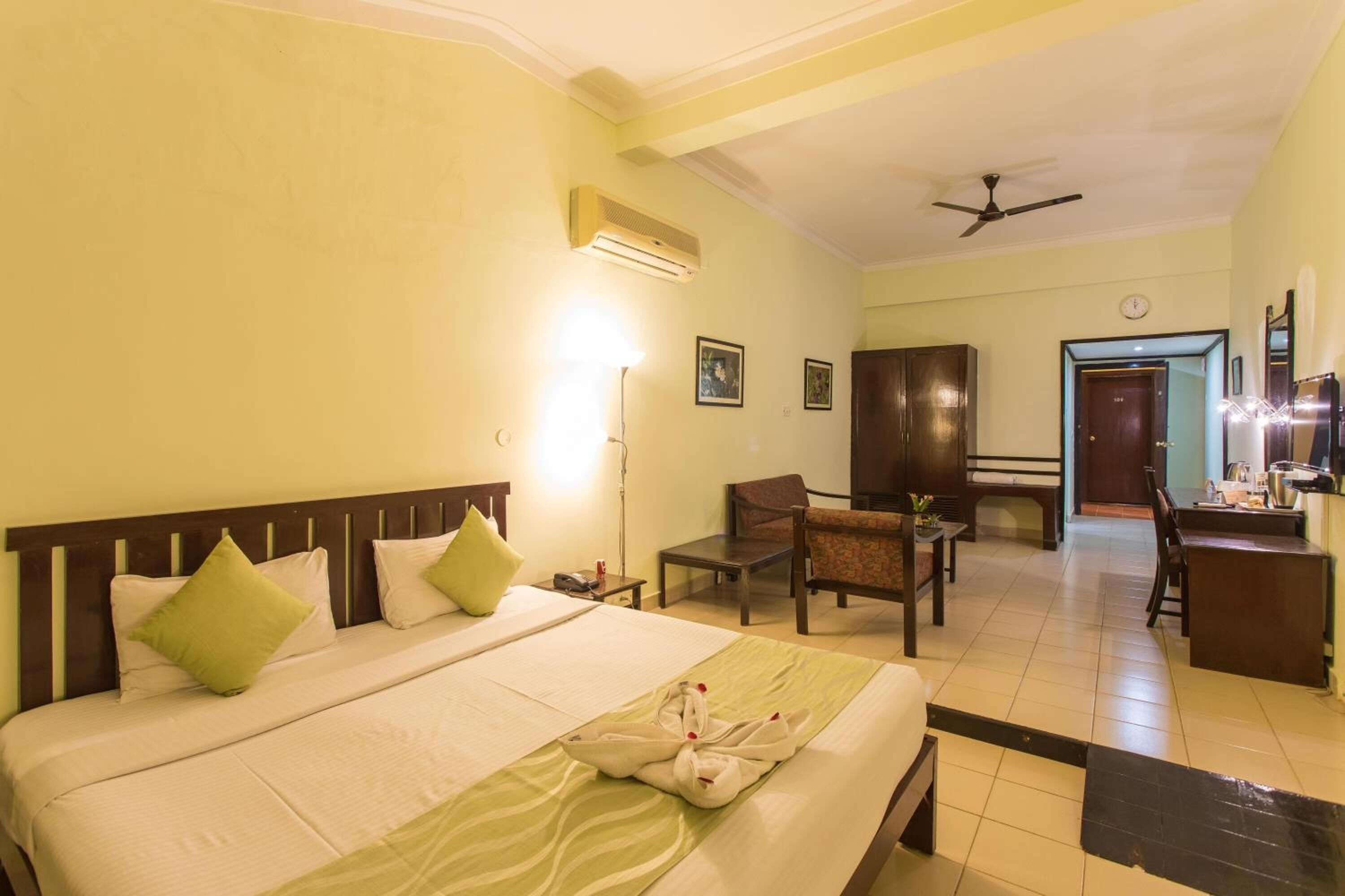 A hotel room with a large bed, a desk, a chair, and a kitchenette.