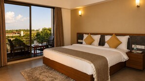 A hotel room with a large bed, a balcony with chairs, and a view of the landscape.