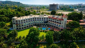 A multi-story hotel with a pool, surrounded by greenery and a cityscape in the background.