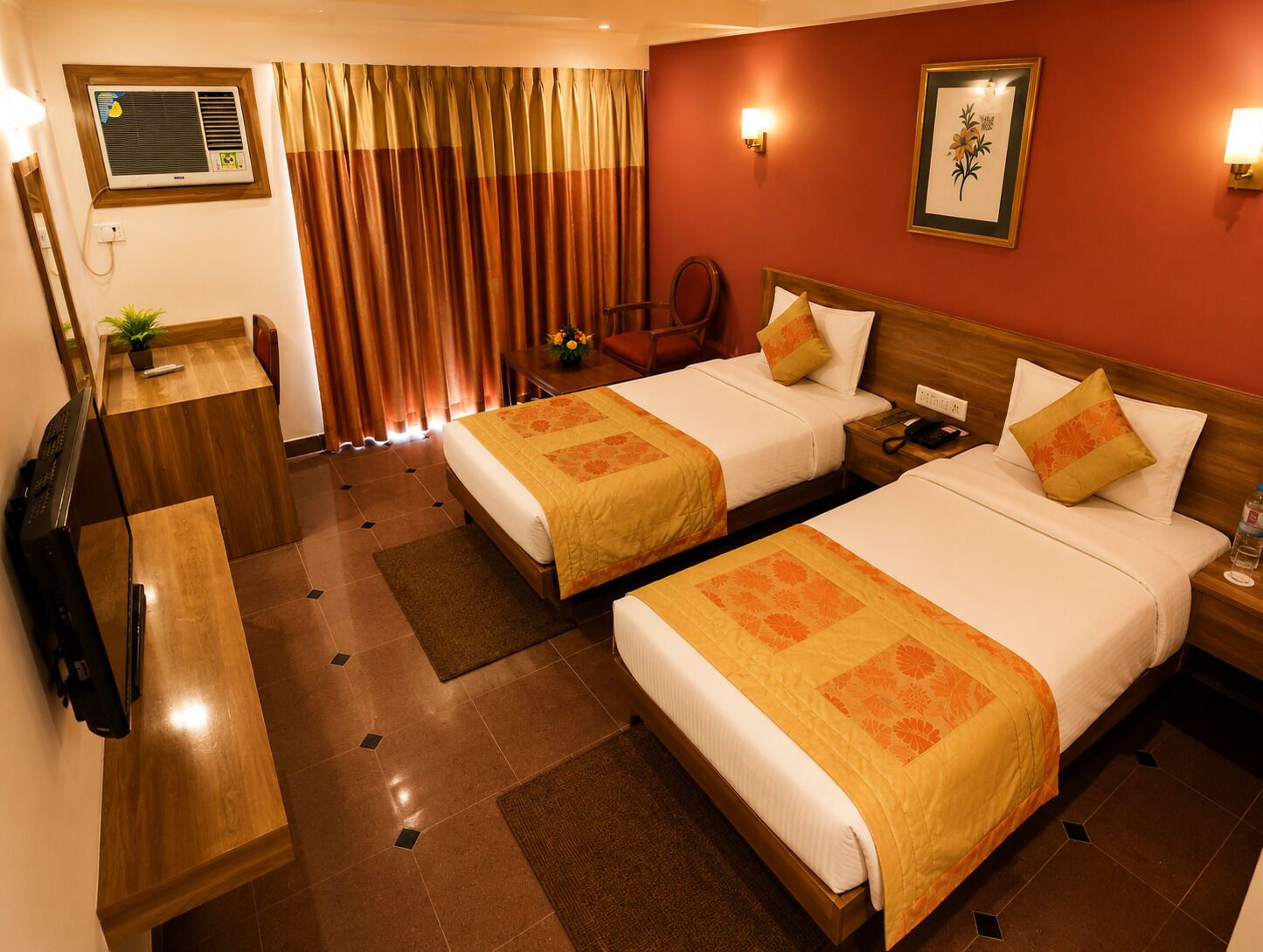 Quarto de hotel com duas camas, uma escrivaninha, uma cadeira, televisão e janela com cortinas.