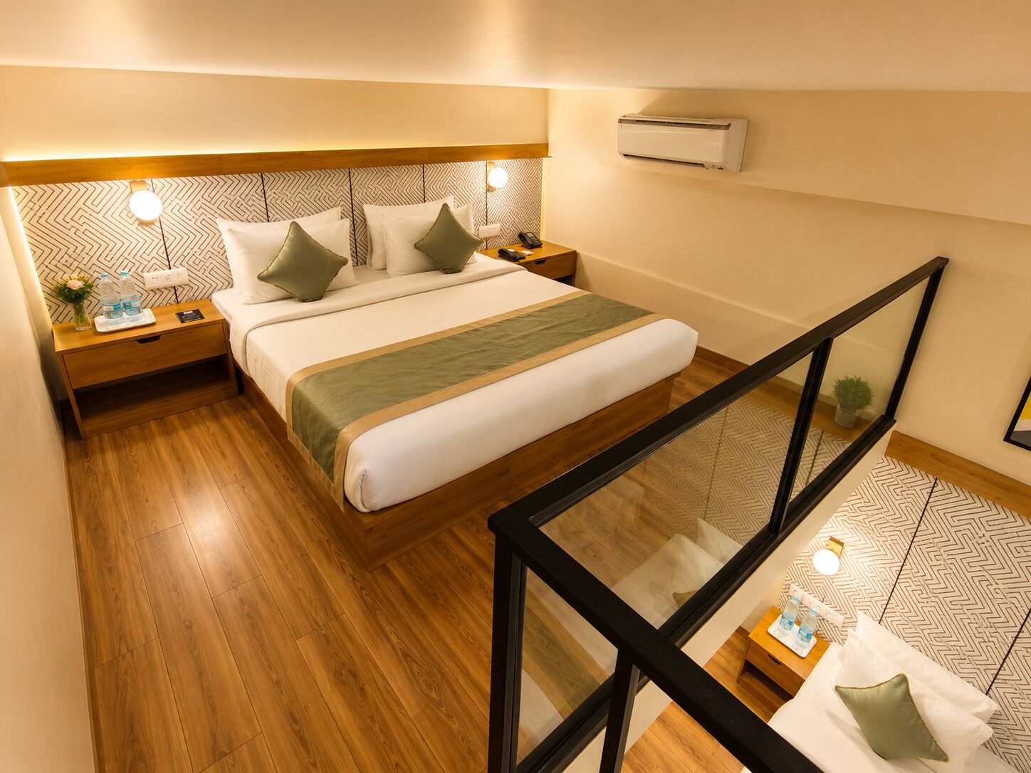 A hotel room with a bed, wooden floor, nightstands, a wall-mounted air conditioner, and a glass railing.