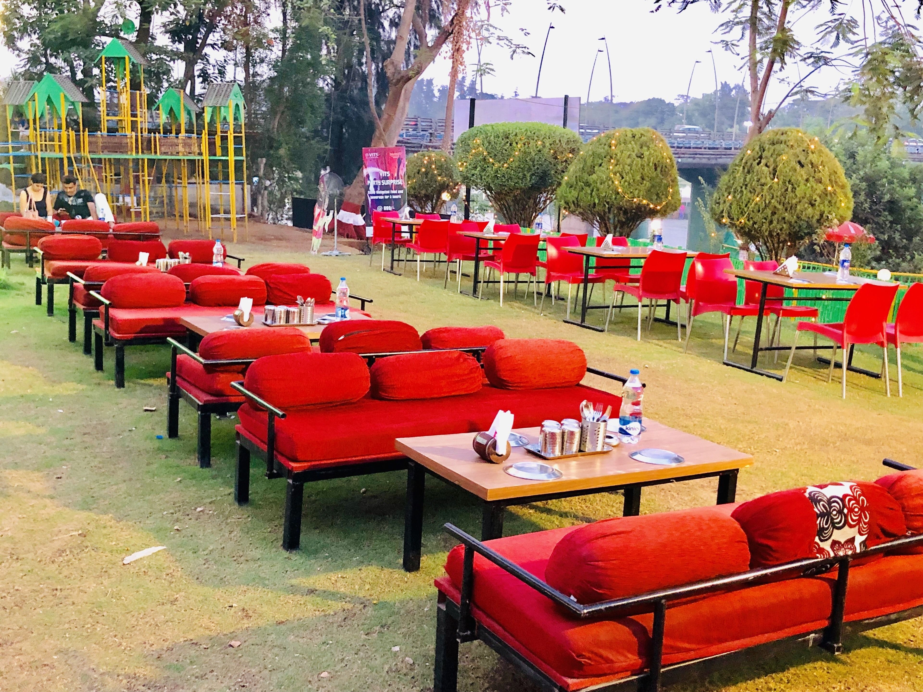 Outdoor seating with red cushions and tables, arranged in rows with a playground in the background.