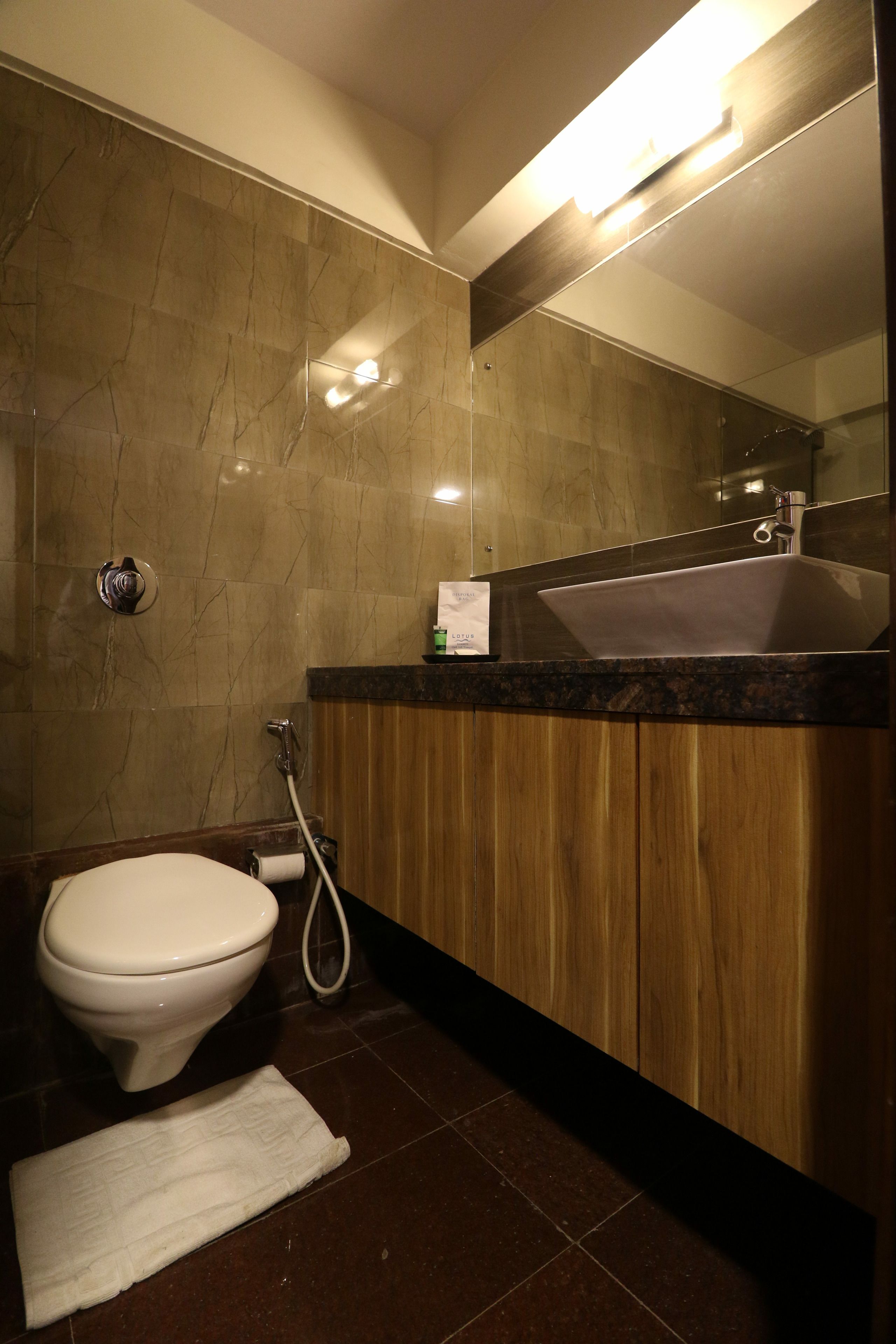 A modern bathroom with a marble wall, a wooden vanity, a sink, and a toilet.