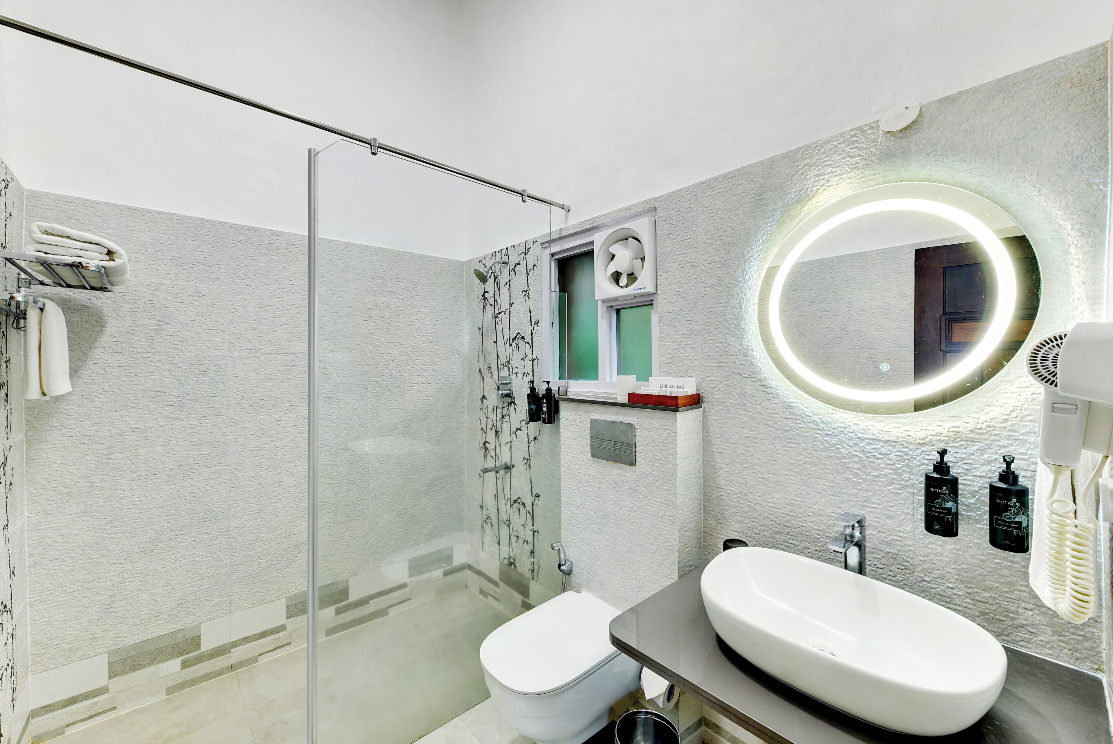 A modern bathroom with a glass shower enclosure, a toilet, a sink with a mirror, and toiletries.