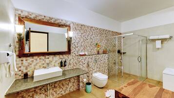 A bathroom with a tiled backsplash, a large mirror, a sink, a toilet, a shower, and a wooden vanity.