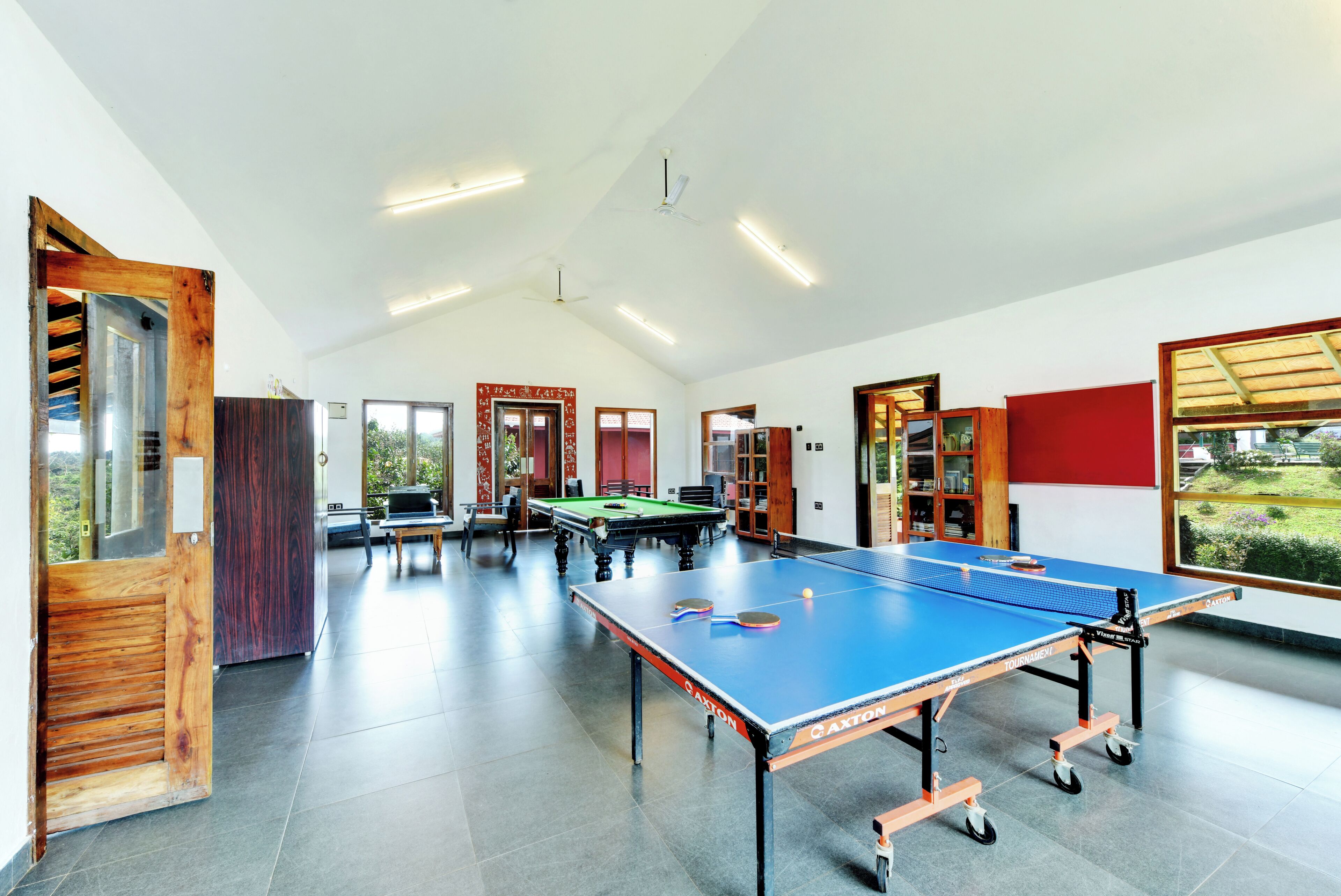Un grand espace intérieur comprenant une table de ping-pong, une table de billard et une table de jeu de flipper.