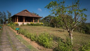 A bungalow with a tiled roof, surrounded by a well-maintained lawn and a variety of shrubs and trees. - Indo Asia Heritage, Coorg (Madikeri)