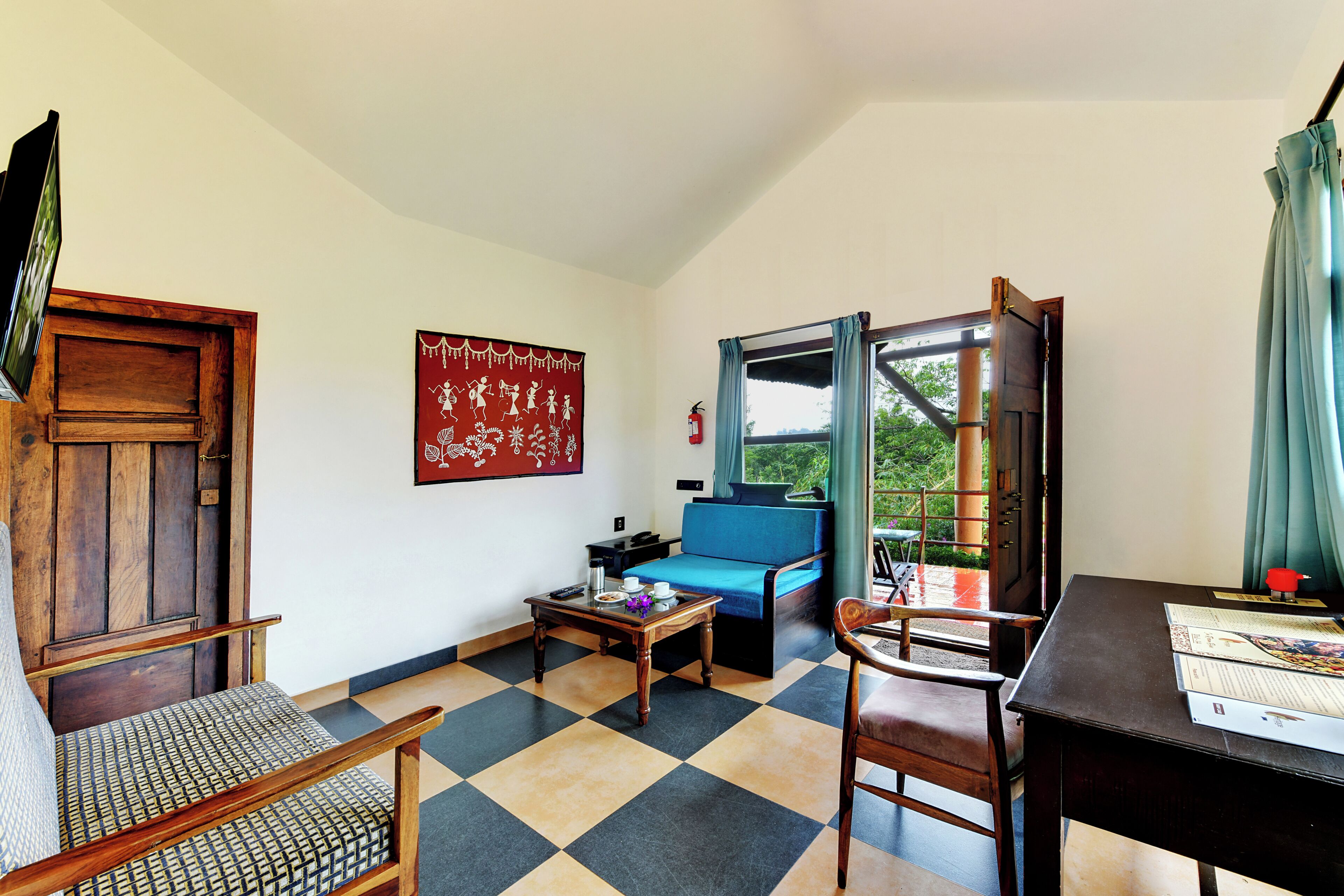 Una habitación con piso a cuadros, un sofá azul, una silla de madera, una mesa con un libro y un tapiz rojo en la pared.