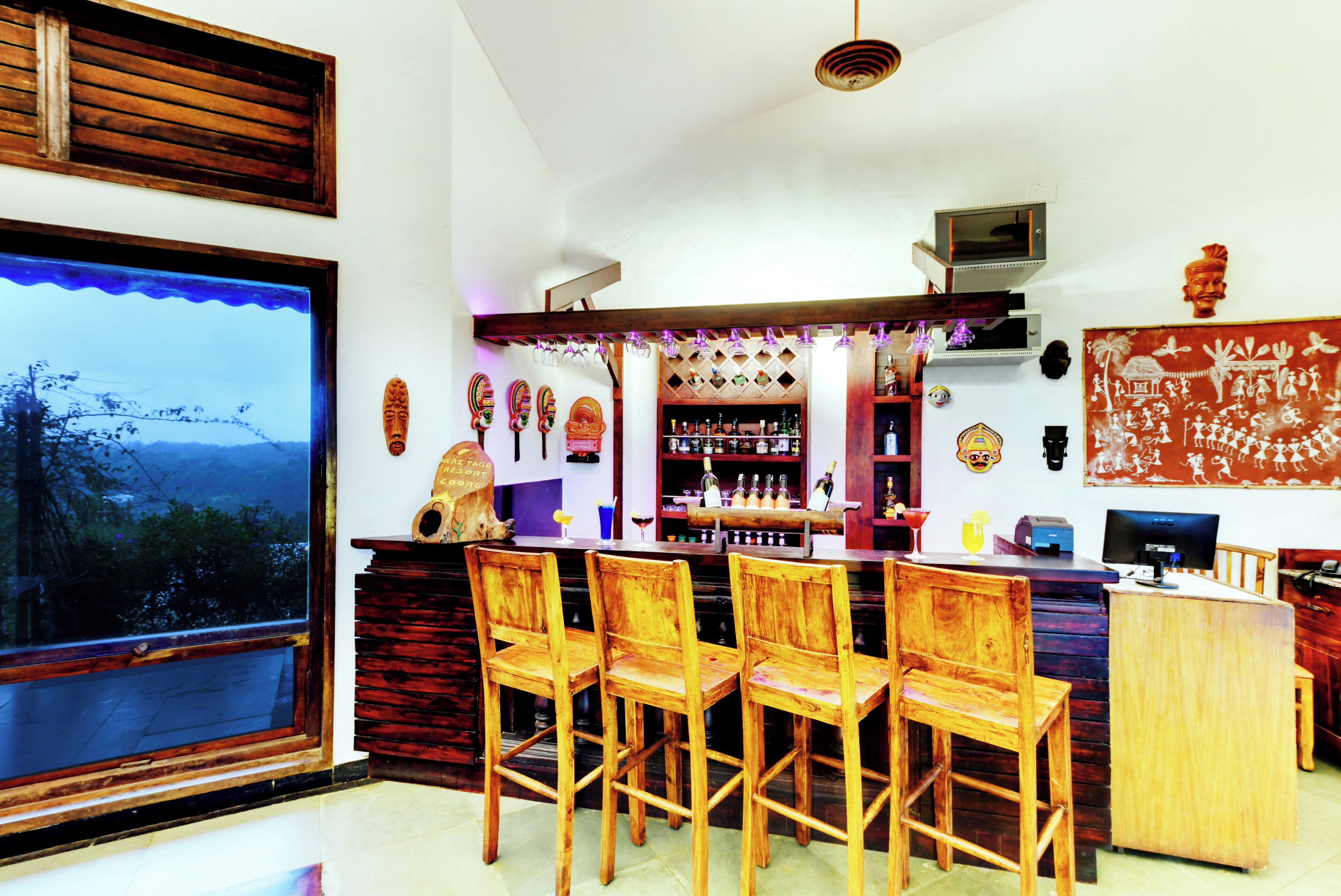 A bar area with wooden chairs, a bar counter, and a view through a large window.