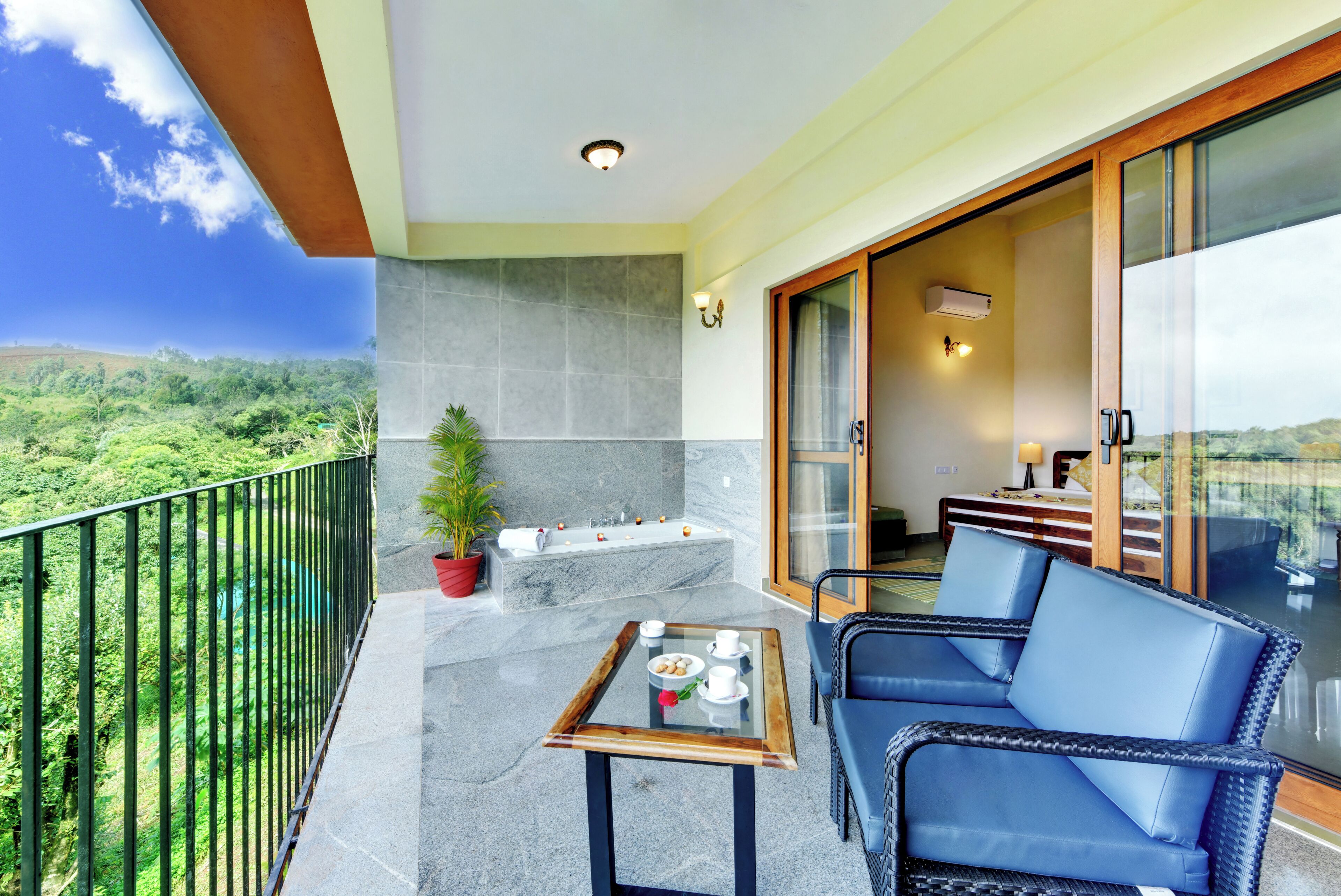 A balcony with a glass table, a potted plant, and a view of a lush landscape.