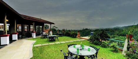 An outdoor seating area with tables and chairs, a covered patio, and a view of the surrounding landscape.