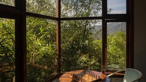 A room with large windows, a wooden chess table, and two chairs. - Indo Asia Heritage, Coorg (Madikeri)