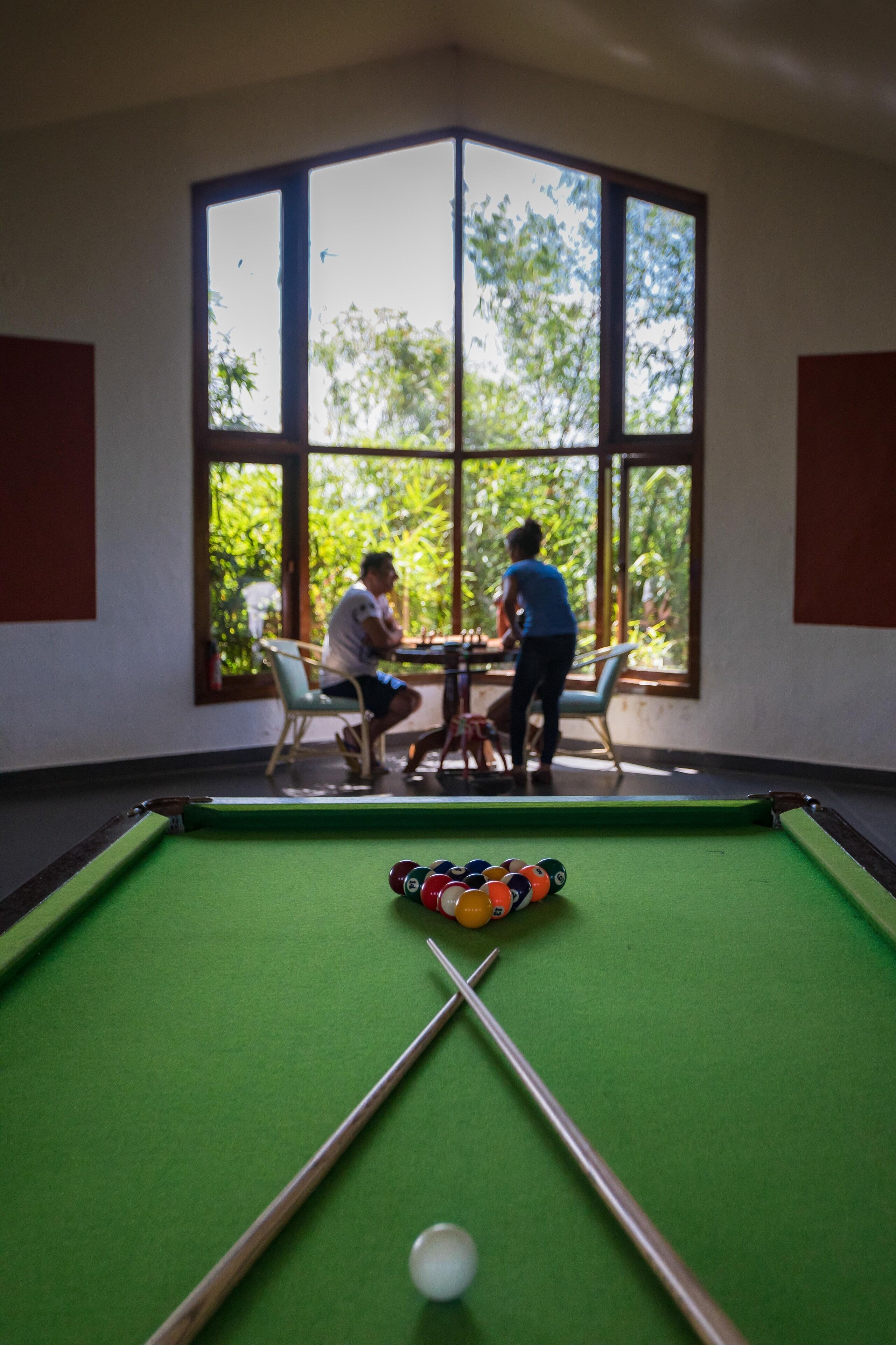 A pool table in a room with large windows, a table, and chairs.