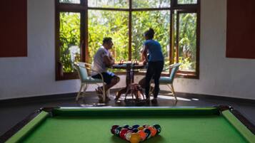 A pool table in a room with large windows, a table, and chairs.