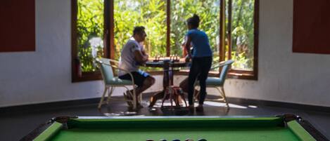 A pool table in a room with large windows, a table, and chairs.