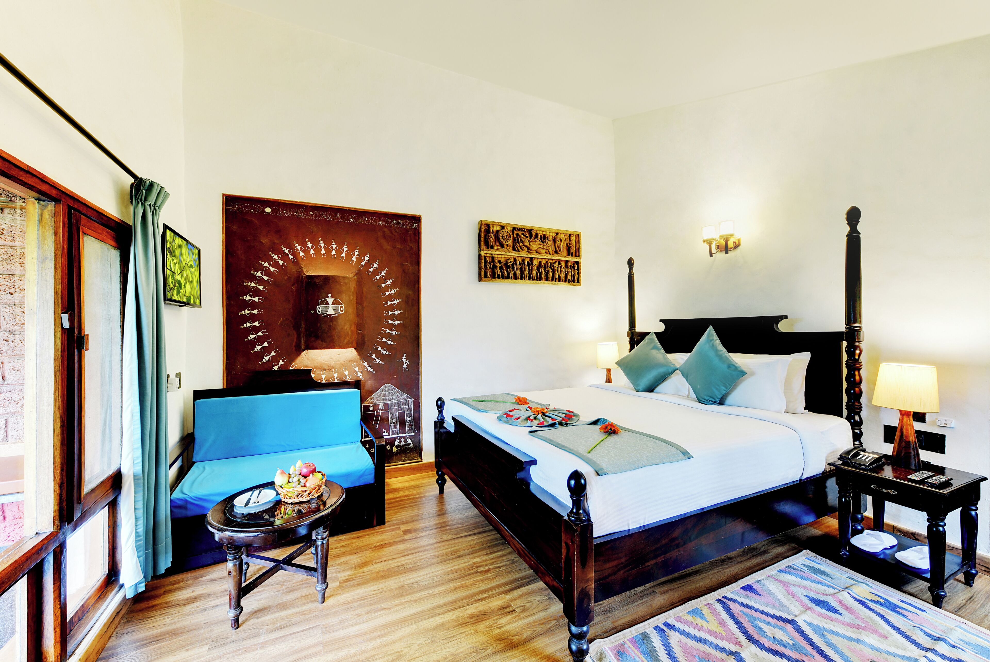 A hotel room with a bed, a sofa, a small table with fruit, a lamp, and a wall with artwork.