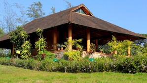 A rustic building with a sloped roof, wooden pillars, and a stone foundation. - Indo Asia Heritage, Coorg (Madikeri)
