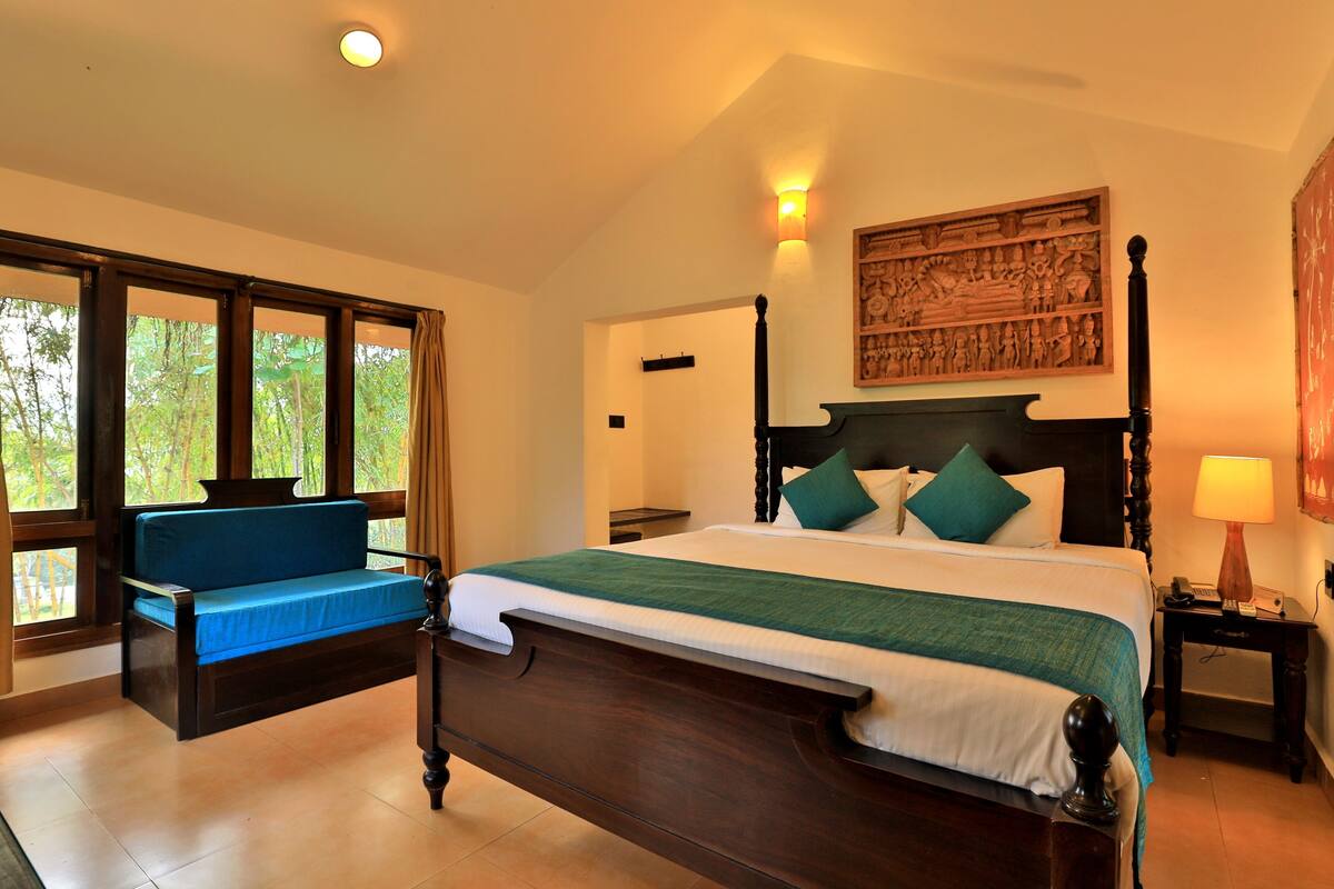 A bedroom with a large bed, a sofa, a nightstand, and a wall-mounted artwork.