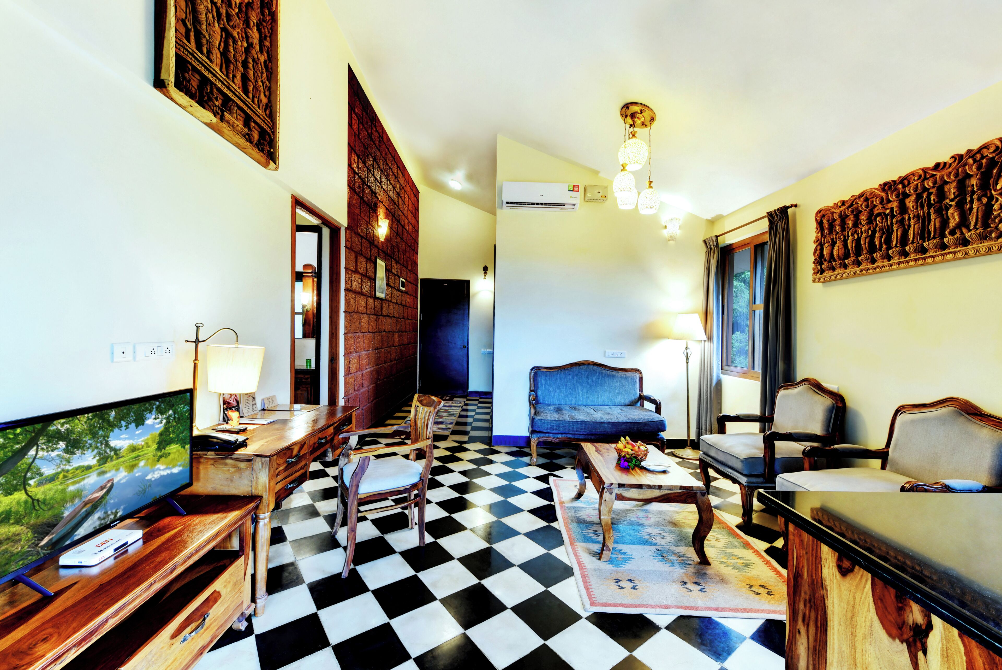 A hotel room with a checkered floor, wooden furniture, a television, and artwork on the walls.