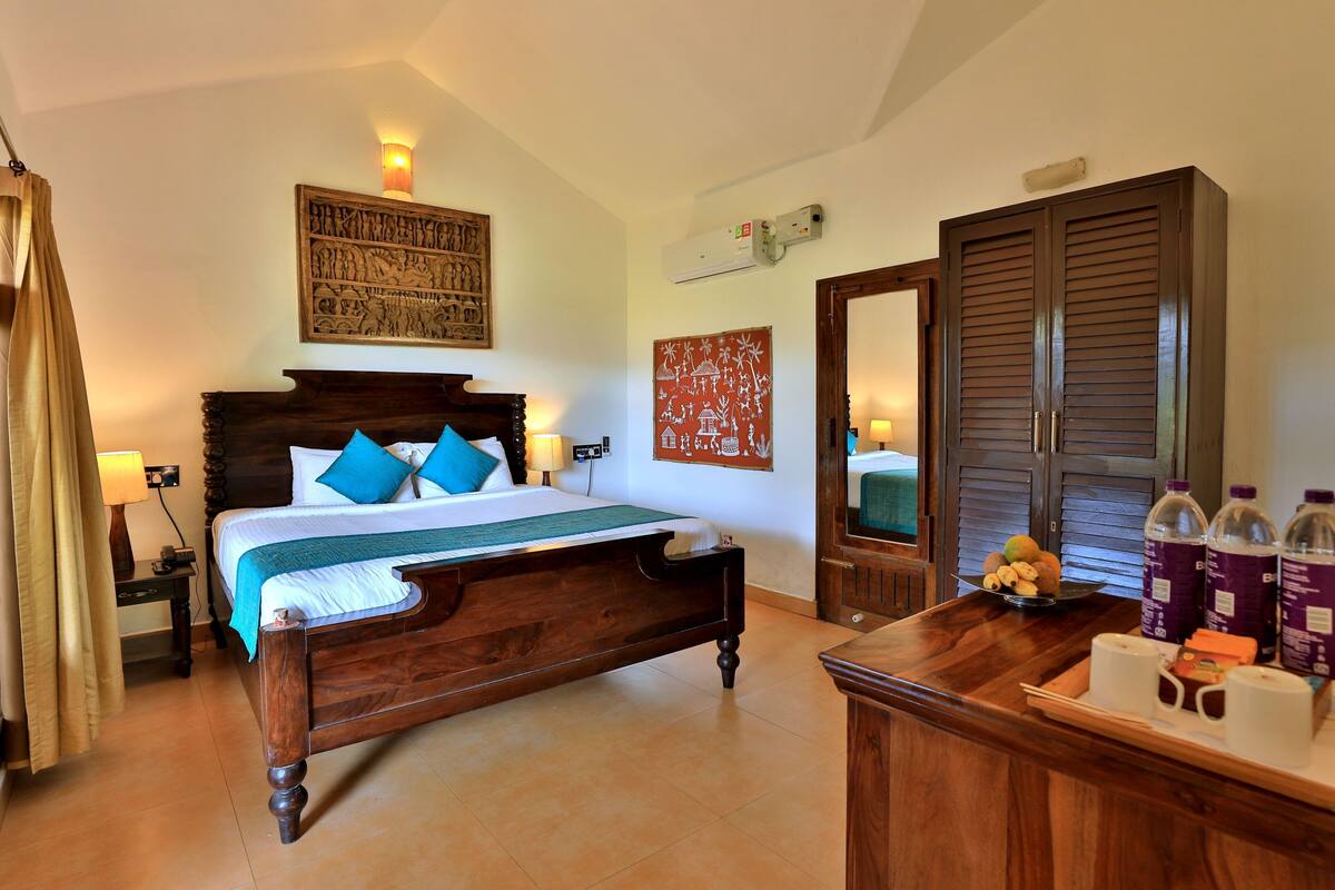 A bedroom with a wooden bed, a nightstand, a bedside table, a mirror, a wardrobe, and a tray with bottles and snacks.