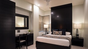 A modern bedroom with a large bed, a desk, and a chair. There is a mirror on the wall and a ceiling fan. - AR Suites Fontana Bay (Pune)