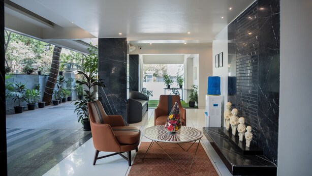 A modern living room with a sofa, armchairs, a coffee table, and decorative items. There are potted plants and a view of the outdoors. - AR Suites Fontana Bay (Pune)