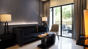 A modern living room with a black sofa, a coffee table, two floor lamps, and a view of the outdoors through large sliding glass doors. - AR Suites Fontana Bay (Pune)