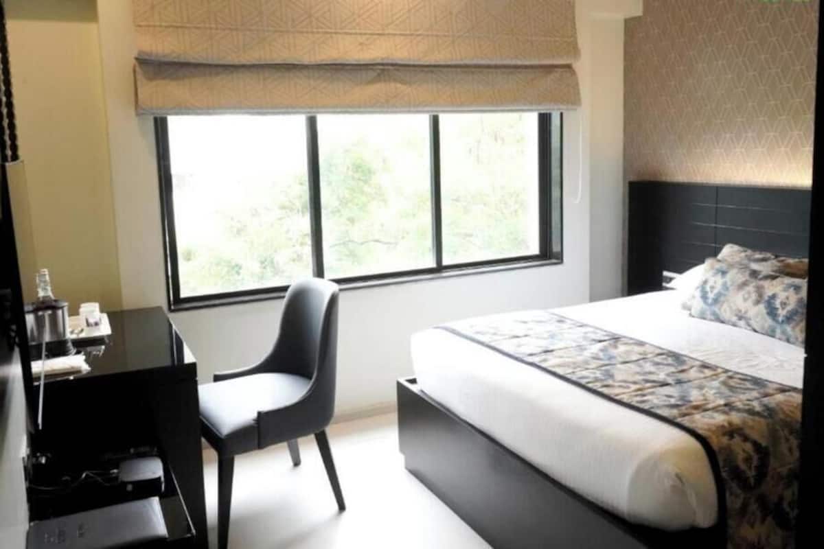 Une chambre d’hôtel équipée d’un lit, d’un bureau, d’une chaise et d’une fenêtre donnant sur un paysage verdoyant.
