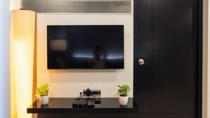 A modern living room with a flat-screen TV mounted on the wall, a black entertainment unit below, and a door to the right. - AR Suites Fontana Bay (Pune)