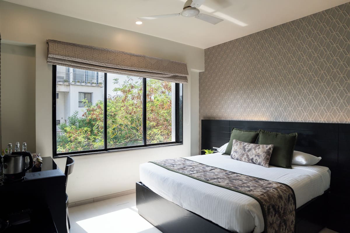 Une chambre moderne avec un grand lit, un bureau et une fenêtre donnant sur un paysage verdoyant.