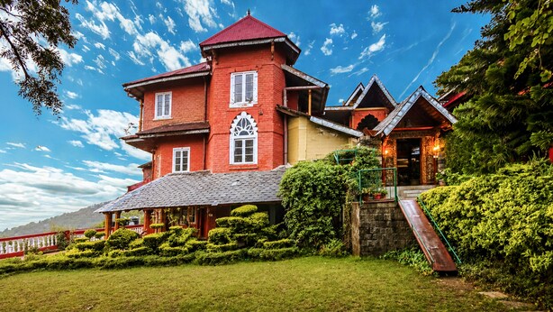 A large, multi-story building with a prominent tower, a covered porch, and a red roof. - WelcomHeritage Grace Hotel (Dharamshala)