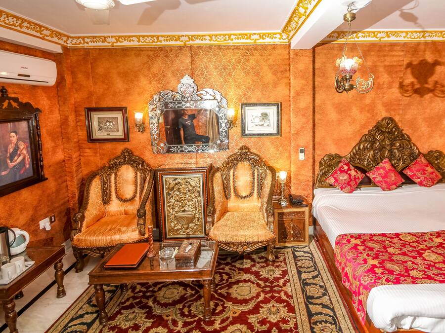 A room with two ornate chairs, a bed with red and gold bedding, and a large mirror.