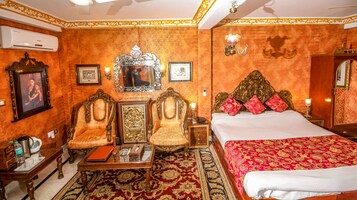 Una habitación con dos sillas decorativas, una cama con ropa de cama roja y dorada, y un espejo grande.