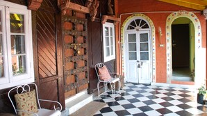 A checkered floor, a wooden door with intricate carvings, and a white chair with a floral cushion. - WelcomHeritage Grace Hotel (Dharamshala)