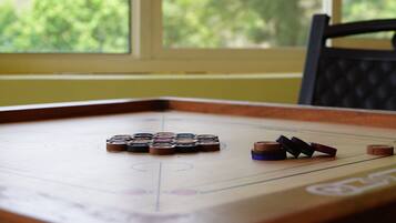 A shuffleboard table with pucks in various colors, positioned near a window with a view of greenery.