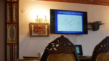 Una sala de conferencias con una pantalla grande que muestra un gráfico de ventas, muebles de madera ornamentados y un cuadro en la pared.