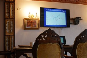 Una sala de conferencias con una pantalla grande que muestra un gráfico de ventas, muebles de madera ornamentados y un cuadro en la pared.