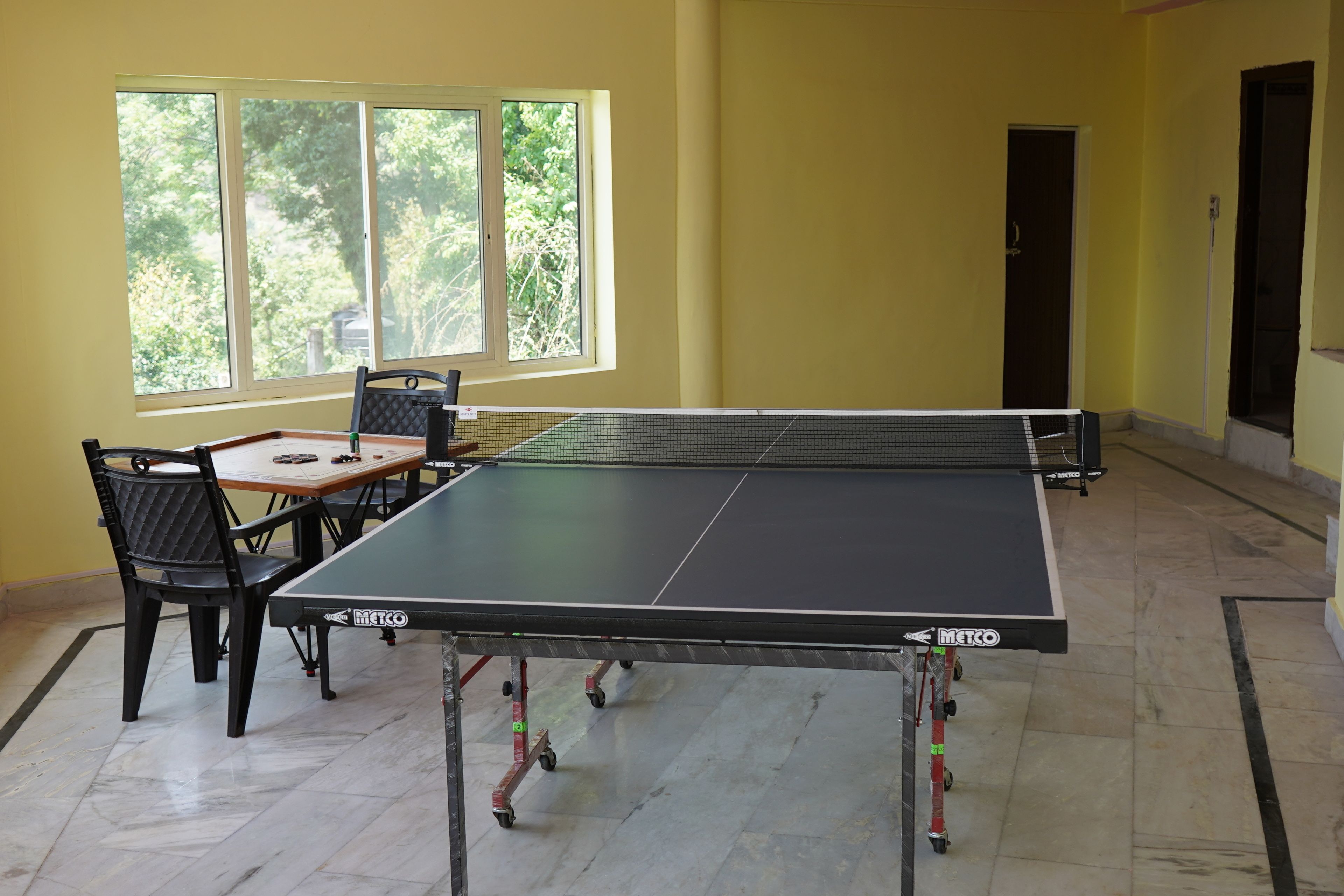 A ping pong table with wheels in a room with yellow walls, a window, and a door.