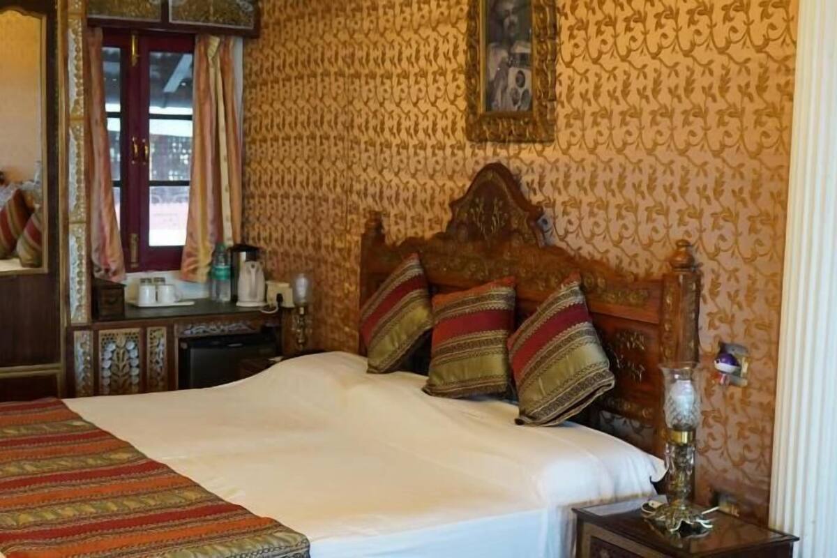 A traditional room with a bed, a mirror, a dresser, and a patterned wall.