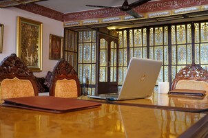 A conference room with a wooden table, two ornate chairs, a laptop, a notebook, and a cup.