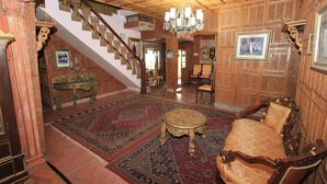 A spacious room with a large wooden staircase, a chandelier, a patterned rug, and a classic wooden sofa. - WelcomHeritage Grace Hotel (Dharamshala)