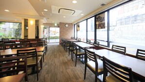 A restaurant with multiple tables and chairs, a brick wall, and large windows. - Smile Hotel Tokyo Ayase Ekimae (Tokyo)