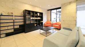 A modern living room with a sofa, two orange chairs, a coffee table, and a large bookshelf filled with books and decorative items. - Smile Hotel Tokyo Ayase Ekimae (Tokyo)