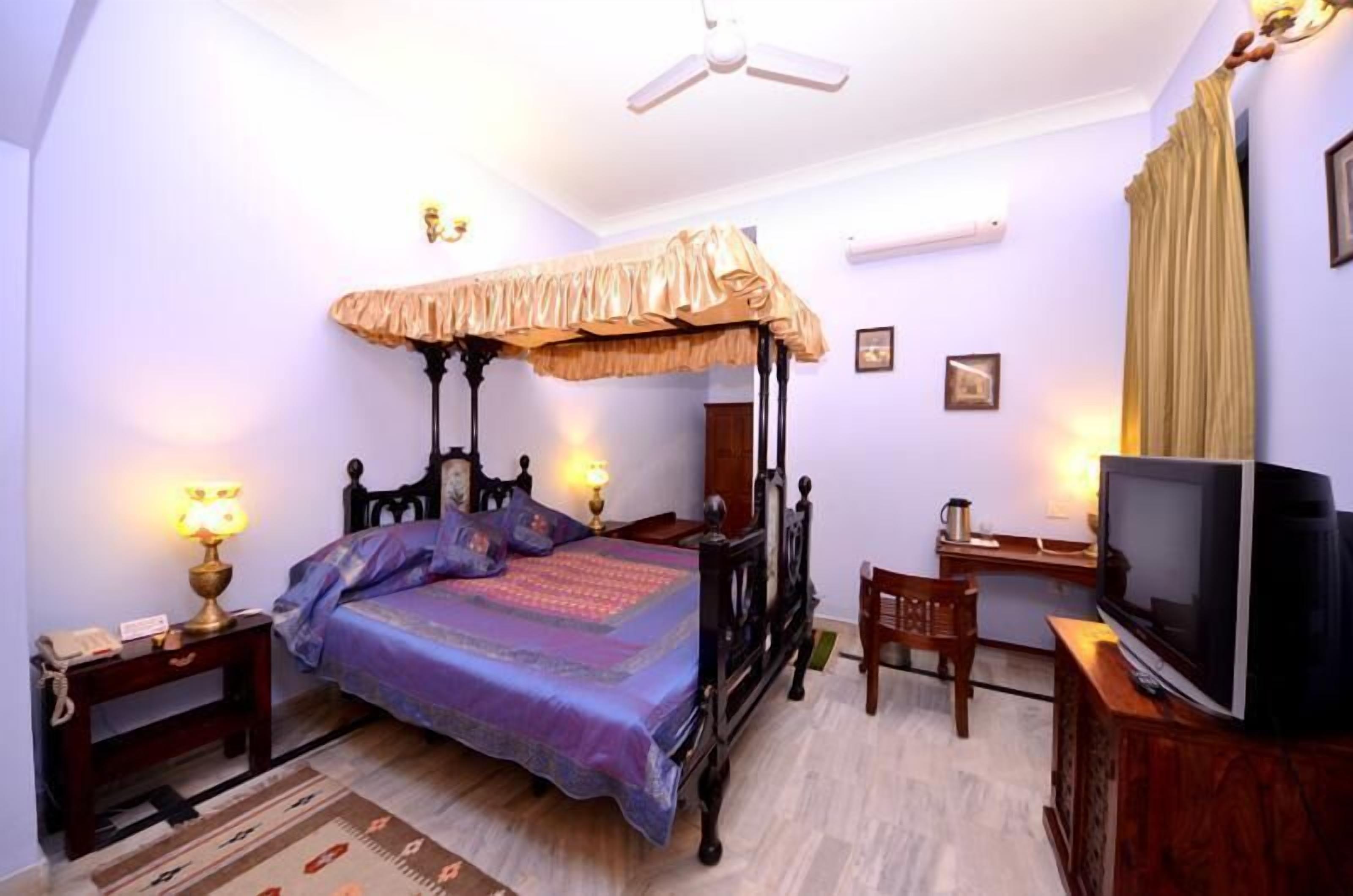 Une chambre à coucher avec un lit à baldaquin, des lampes de chevet, une télévision et un bureau avec une chaise.
