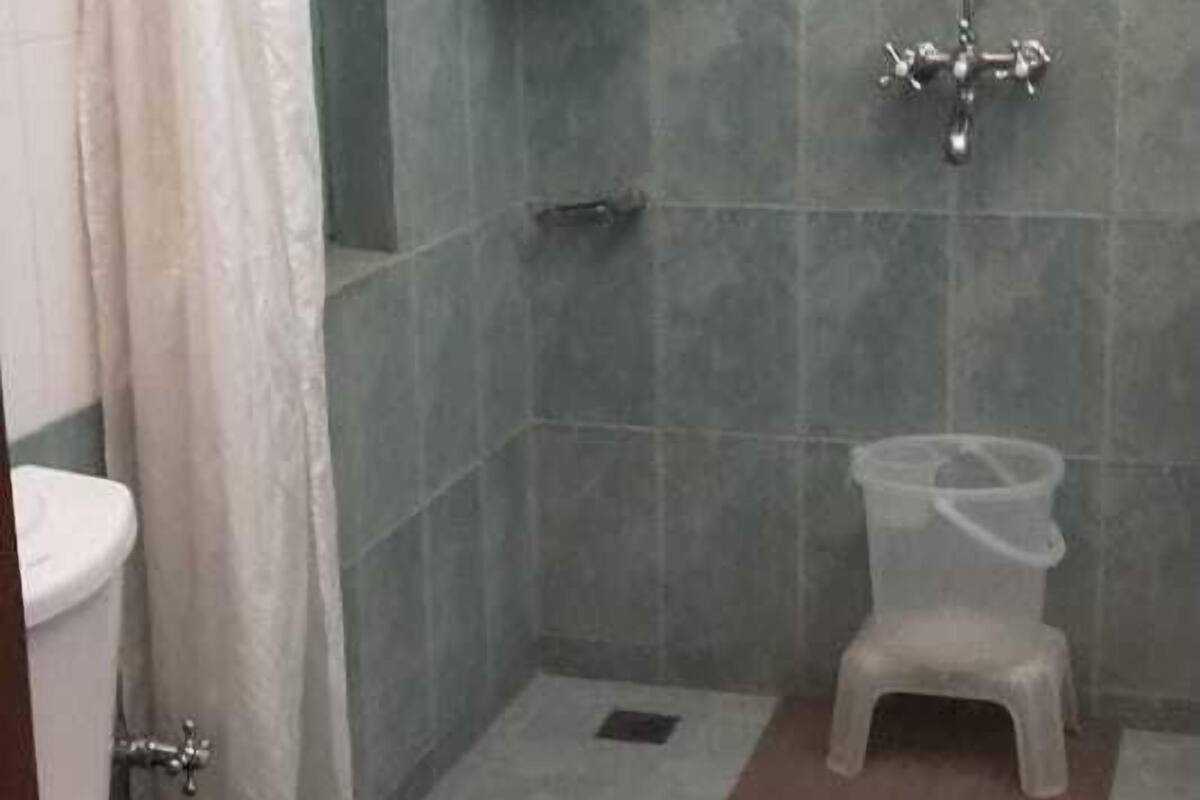 A bathroom with a shower, toilet, and a small stool.