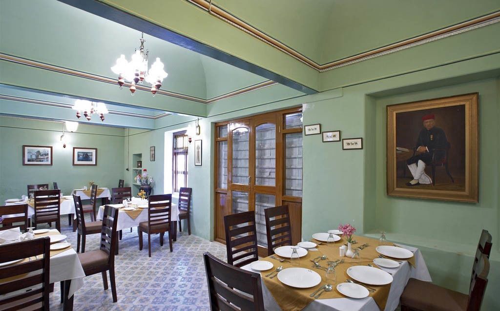Un comedor con mesas dispuestas para cuatro personas, sillas de madera y una araña.