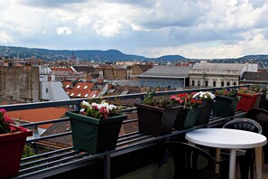 A terrace with a table and chairs, overlooking a cityscape with buildings and a mountain in the distance. - Silver Hotel Budapest City Center (Budapest)